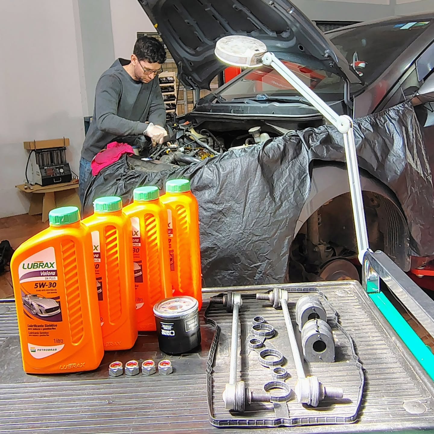Técnico da Excelência realizando serviço no motor com produtos Lubrax e capa protetora no veículo
